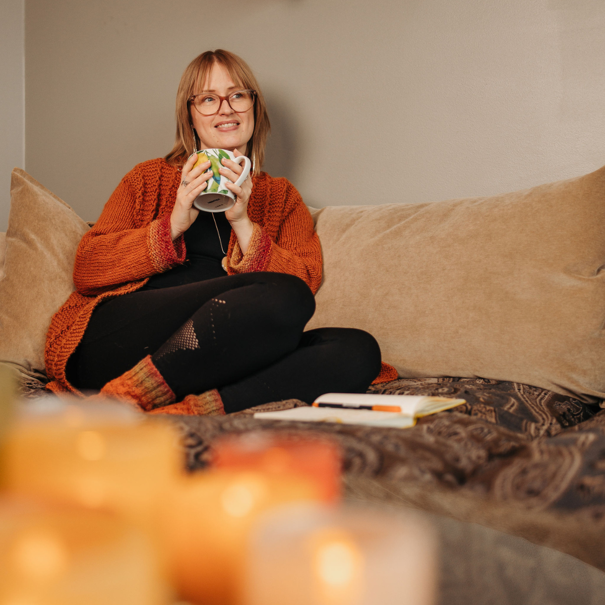 anna sitter i soffan och håller en tekopp i handen med ett anteckningsblock framför sig